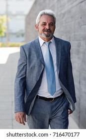 Senior Businessman Walking Outside Of Modern Office Building. Successful Business Man Wearing Formal Suit And Tie In Urban Background.