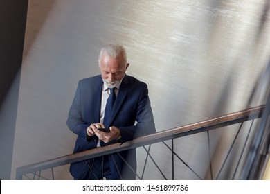 Senior Businessman Walking Up The Stairs In A Modern Office Building, Going To His Workplace And Typing A Text Message