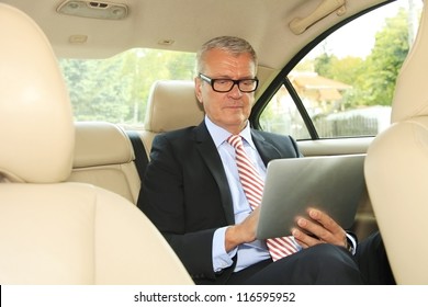 Senior Businessman Working In Back Of Car And Using A Tablet