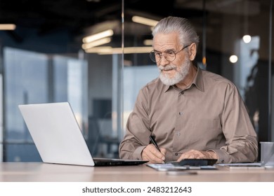 Senior businessman working on a laptop and taking notes in a modern office. The image captures a mature professional in a work environment, showcasing productivity, experience, and dedication - Powered by Shutterstock