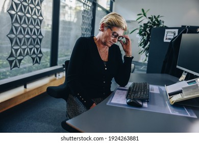 Senior businesswoman looking tired sitting at her desk. Female professional feeling stressed while working in office. - Powered by Shutterstock