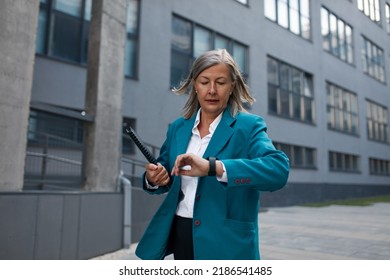 Senior Businesswoman Office Worker Looking Time On Hand Watch. Lady Walking Through The Street In Urban City. Business Woman Go To Working At Office Building District In Morning Rush Hour 