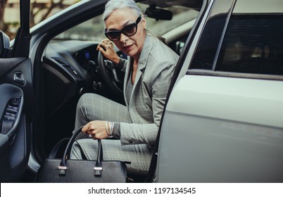 Senior Businesswoman With Purse Getting Out Of Her Car. Sophisticated Mature Woman Disembarking The Car.