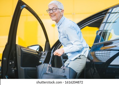 Senior Businesswoman With Purse Getting Out Of Her Car. Sophisticated Mature Woman Disembarking The Car.