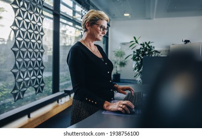 Senior Businesswoman Working At Standing Desk. Woman Employee Working On Desktop Computer At Ergonomic Standing Desk.