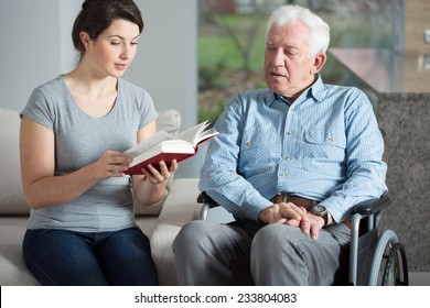 Senior care assistant reading book elderly man