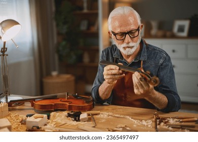 Senior carpenter craftsman carving wood and making violin instrument - Powered by Shutterstock