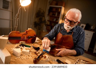 Senior carpenter craftsman carving wood and making violin instrument - Powered by Shutterstock