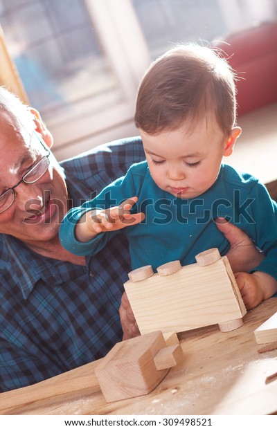 Senior carpenter and his grandson working\
in the workshop, they make a wooden toy\
car.