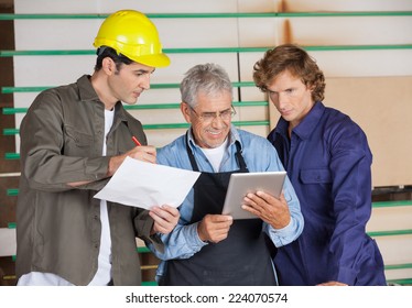 Senior carpenter holding tablet computer while communicating with colleagues in workshop - Powered by Shutterstock