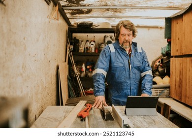 Senior carpenter man looking at his ipad. Carpenter man start working on his wood workshop. Skilled senior carpenter man watching woodwork tutorial on ipad. - Powered by Shutterstock