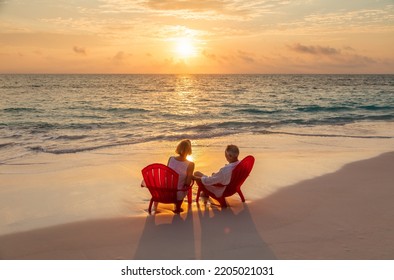 Senior Caucasian American couple with carefree lifestyle relaxing on red chairs by the ocean at sunrise Bahamas - Powered by Shutterstock