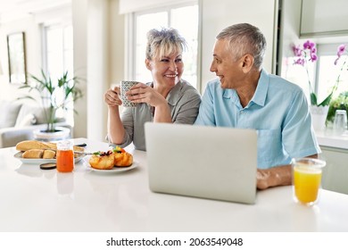 Senior caucasian couple having breakfast using laptop at the kitchen. - Shutterstock ID 2063549048