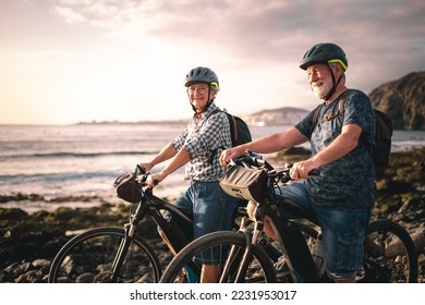 Senior caucasian couple riding off road on the pebble beach with electric bicycles at sunset. Authentic elderly retired life and sustainable mobility concept - Powered by Shutterstock