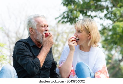 Senior caucasian couple sitting on field grass and enjoy eating apple together outdoors in parks. Happy mature couple eating fruits in a summer park. Healthy and lifestyle retired couple outdoors. - Shutterstock ID 2043966002