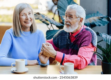 Senior Caucasian couple sitting together at cafe holding hands and smiling. Joyful elderly man and woman enjoying connection, love, simple joys and companionship in golden years. - Powered by Shutterstock