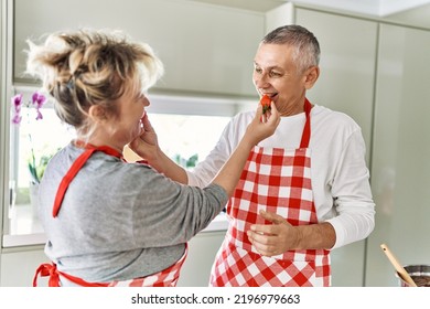 Senior caucasian couple smiling happy giving strawberry to each other at the kitchen.