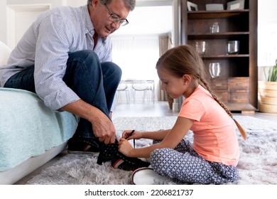 Senior Caucasian Father Sitting On A Couch, His Granddaughter Tying His Shoes For Him. Family And Older People.