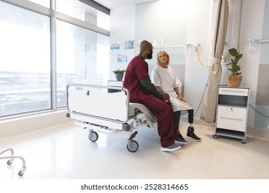 Senior caucasian female patient with prosthetic leg and african american male doctor sitting on bed. Hospital, disability, medicine and healthcare, unaltered. - Powered by Shutterstock