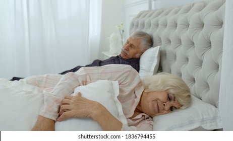 Senior Caucasian grandparents couple lying and sleeping in bed at home. Irritated woman getting disturbed with man loudly snoring - Powered by Shutterstock