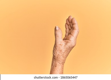 Senior caucasian hand over yellow isolated background picking and taking invisible thing, holding object with fingers showing space 