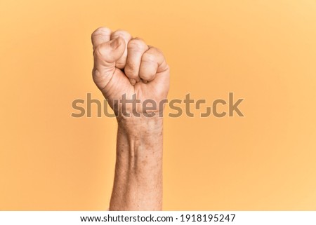 Senior caucasian hand over yellow isolated background doing protest and revolution gesture, fist expressing force and power 