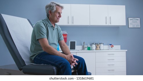 Senior Caucasian male patient waiting for doctor while sitting on exam room table. Older man going to regular appointment for annual check up