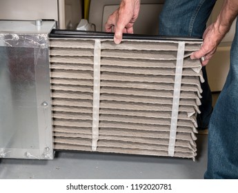 Senior Caucasian Man Changing A Folded Dirty Air Filter In The HVAC Furnace System In Basement Of Home