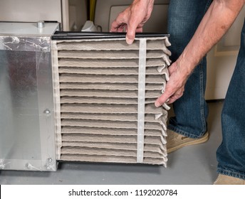 Senior Caucasian Man Changing A Folded Dirty Air Filter In The HVAC Furnace System In Basement Of Home