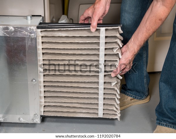 Stock photo showing a man removing a dirty air filter from furnace and HVAC system