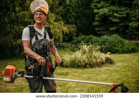 Senior caucasian man farmer gardener standing in the field with a string trimmer