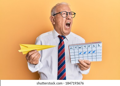 Senior Caucasian Man Going On Business Trip Holding Paper Airplane Angry And Mad Screaming Frustrated And Furious, Shouting With Anger. Rage And Aggressive Concept. 