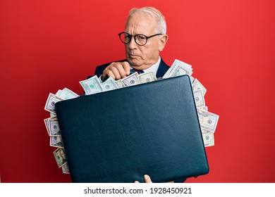 Senior Caucasian Man Holding Briefcase Full Of Dollars Skeptic And Nervous, Frowning Upset Because Of Problem. Negative Person. 