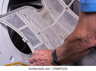 Senior caucasian man holding the lint filled trap from a front loading tumble dryer