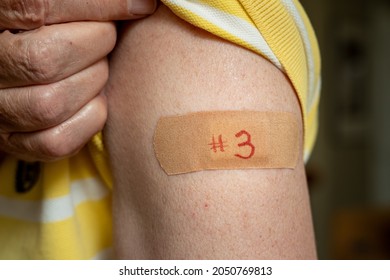 Senior caucasian man holding up shirt sleeve to show the bandaid after the booster coronavirus vaccine shot in the shoulder