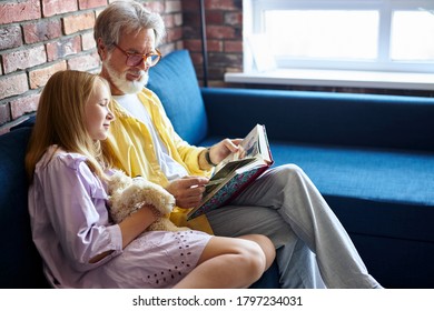 senior caucasian man and little girl looking at family photo album in living room, family concept