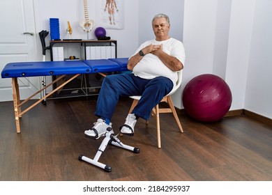 Senior Caucasian Man At Physiotherapy Clinic Using Pedal Exerciser Smiling With Hands On Chest With Closed Eyes And Grateful Gesture On Face. Health Concept. 