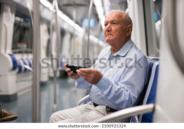 Senior Caucasian man with smartphone sitting on seat\
in subway car.