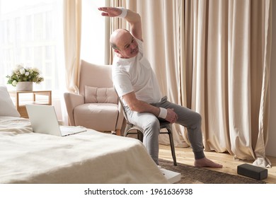 Senior caucasian man stretching side sitting on chair at his living room.