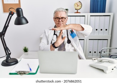Senior caucasian man wearing doctor uniform and stethoscope at the clinic doing time out gesture with hands, frustrated and serious face 