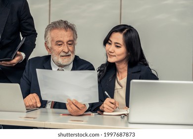 Senior Caucasian Manager Working In Office With Assistance Of Young Asian Business People And Translator In The Meeting. Corporate International Business And Secretary Language Translation Concept.