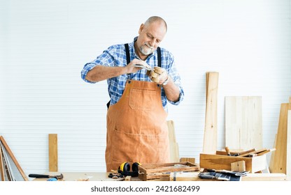 Senior Caucasian retired old male woodworker, carpenter reading, rechecking and comparing drawing plan with finish wooden figure toy or furniture before giving to customer. Hobby, Retirement Concept - Powered by Shutterstock