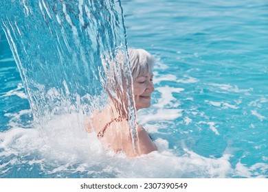 Senior caucasian smiling woman with gray hair enjoying falling on her shoulders flow of water. Hydromassage in outdoor thermal swimming pool. Active elderly concept. Blurry movement - Powered by Shutterstock