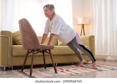 Senior caucasian woman doing yoga at home on chair - Powered by Shutterstock