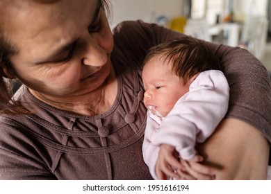 Senior caucasian woman grandmother hold newborn infant girl vomiting milk - baby overfeeding puke milk in hands of her granny at home - new life nursing and growing up concept