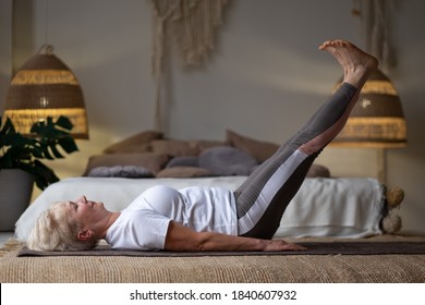 Senior Caucasian Woman Lying On Mat With Legs Up At Home.