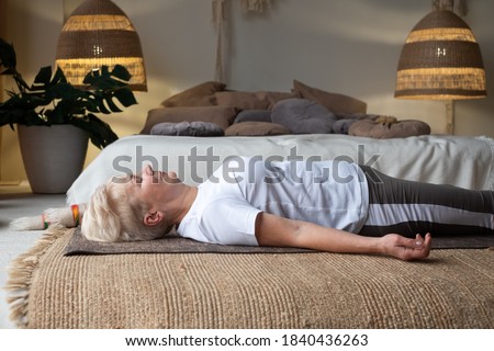 Senior caucasian woman lying on yoga mat after workout. Fit female relaxing on floor at home.