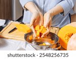 Senior Caucasian woman puts chopped pieces of ripe pumpkin in saucepan 