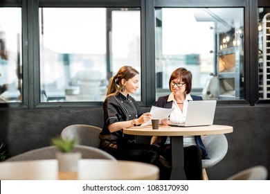 Senior chef and young cook working on the new menu or recipe sitting in the cafe or restaurant near the kitchen - Powered by Shutterstock