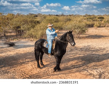 senior citizen with a beard and a cowboy hat dressed in denim, mounted on a black horse, leading the way , pointing to directions, on a horseback safari 